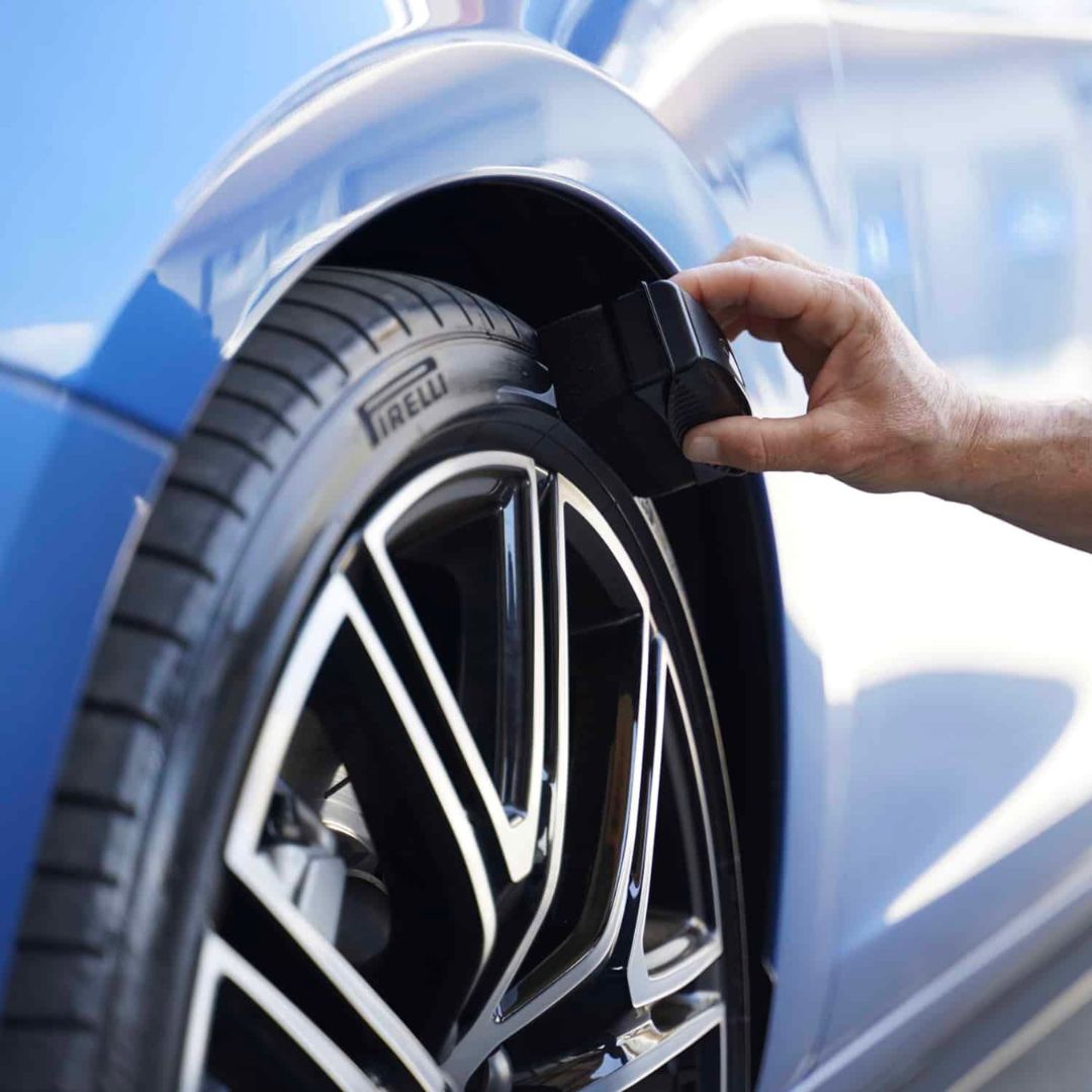 Person applying tire sealant to a car tire with a blue car in the background