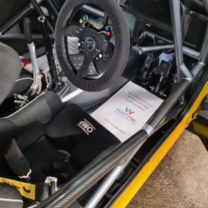 Close-up of a race car interior with steering wheel and dashboard, featuring a washme.ie paper mat.